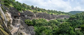 Eine beeindruckende Reihe von Höhlen, in Fels gemeißelt, eingebettet in eine grüne Hügellandschaft, mit Zugangswegen, die durch die steilen Klippen führen.