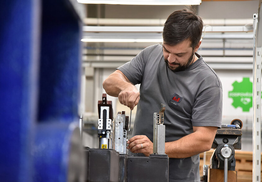 Ein Metalltechniker bei weba Werkzeugbau in Aktion, konzentriert auf den Zusammenbau von Messaufnahmen in der Produktionshalle. Der Techniker, in sauberer und praktischer Arbeitskleidung, arbeitet präzise an einem gut beleuchteten Arbeitstisch. Umgeben von verschiedenen Werkzeugen und Bauteilen, zeigt das Bild den Detailreichtum und die Präzision, die im Werkzeugbau erforderlich sind. Die Szene vermittelt ein Gefühl von Fachwissen und Engagement im Produktionsprozess, charakteristisch für die hohe Qualitätsstandards bei weba. Das Bild steht symbolisch für Jobs in Steyr für Berufserfahrene und Profis bei weba Werkzeugbau.