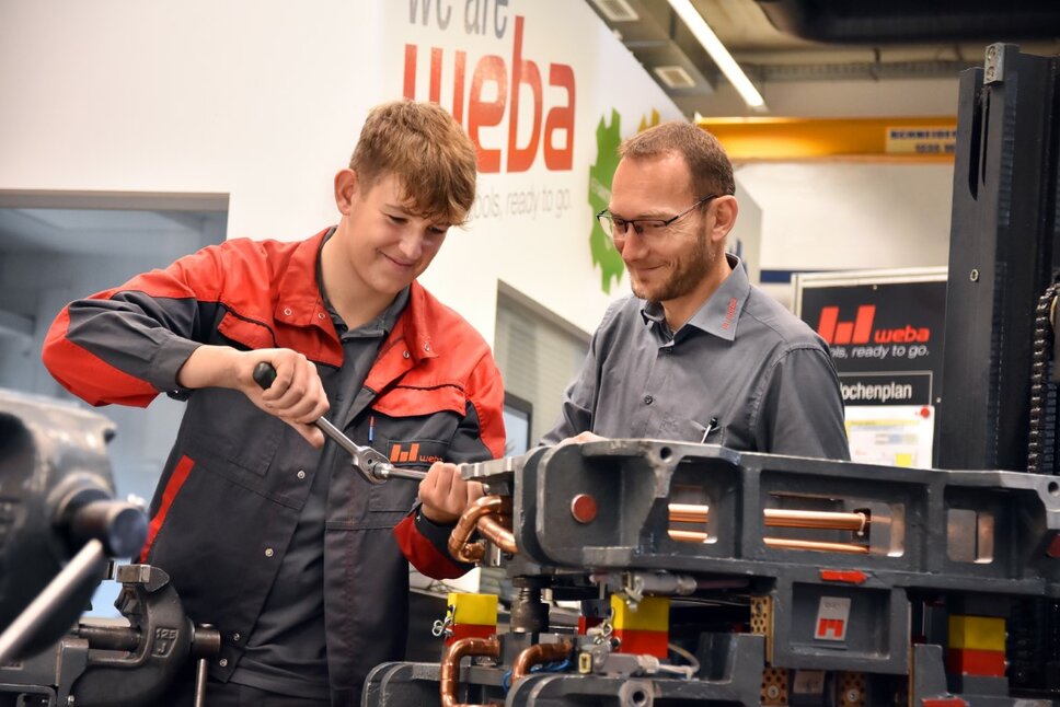 Ein Lehrling in der Werkzeugbautechnik arbeitet an einer Miniatur eines Umformwerkzeugs, während der Ausbilder aufmerksam zuschaut.