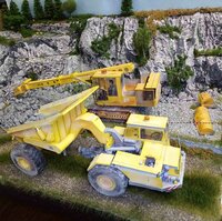 Detailní modelářská scéna se žlutými stavebními stroji před skalnatou krajinou.