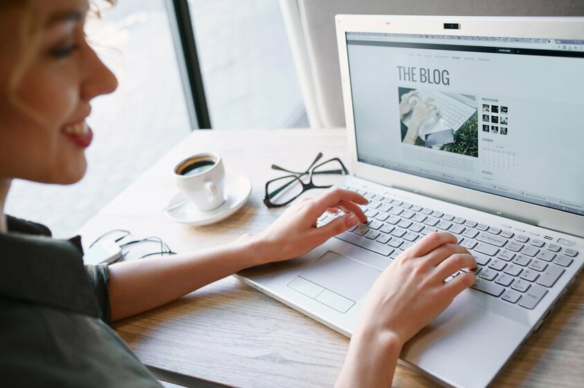 Foto einer Frau, die konzentriert an einem Laptop arbeitet. Auf dem Bildschirm des Laptops ist deutlich "The Blog" zu sehen, was darauf hindeutet, dass sie entweder an einem Blogbeitrag schreibt oder Bloginhalte durchstöbert.