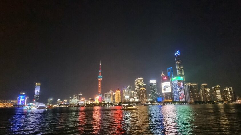 Nächtlicher Blick auf die beleuchtete Skyline von Shanghai mit farbig reflektierenden Lichtern auf dem Wasser – ein Highlight aus Jan Wengryns Zeit in China.