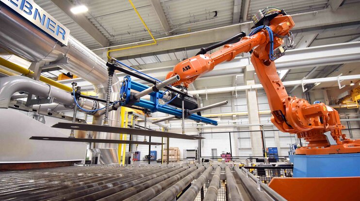 An industrial robot lifts heated sheet blanks in a modern hot forming system to prepare them for the forming process.